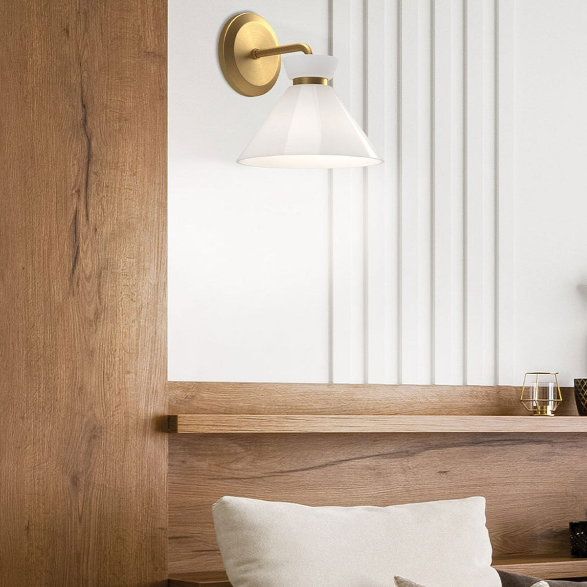 A brass wall light with a white conical shade installed above a wooden headboard.