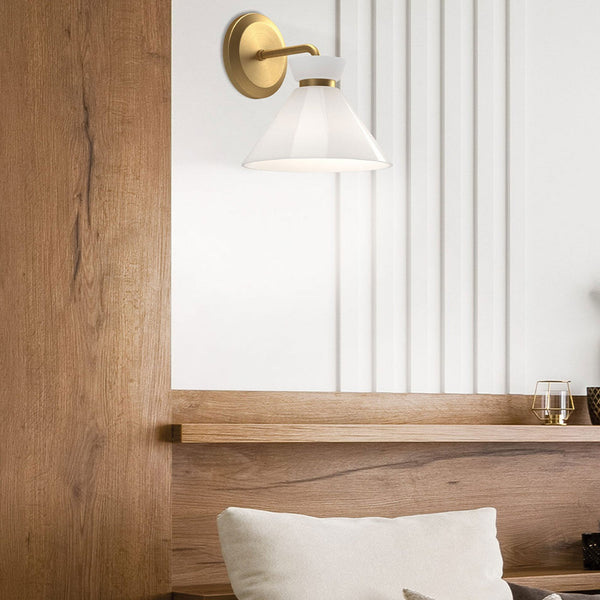 A brass wall light with a white conical shade installed above a wooden headboard.