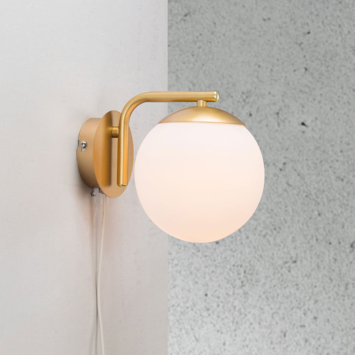 A close-up of a wall light with a frosted globe and brass fitting on a grey wall.
