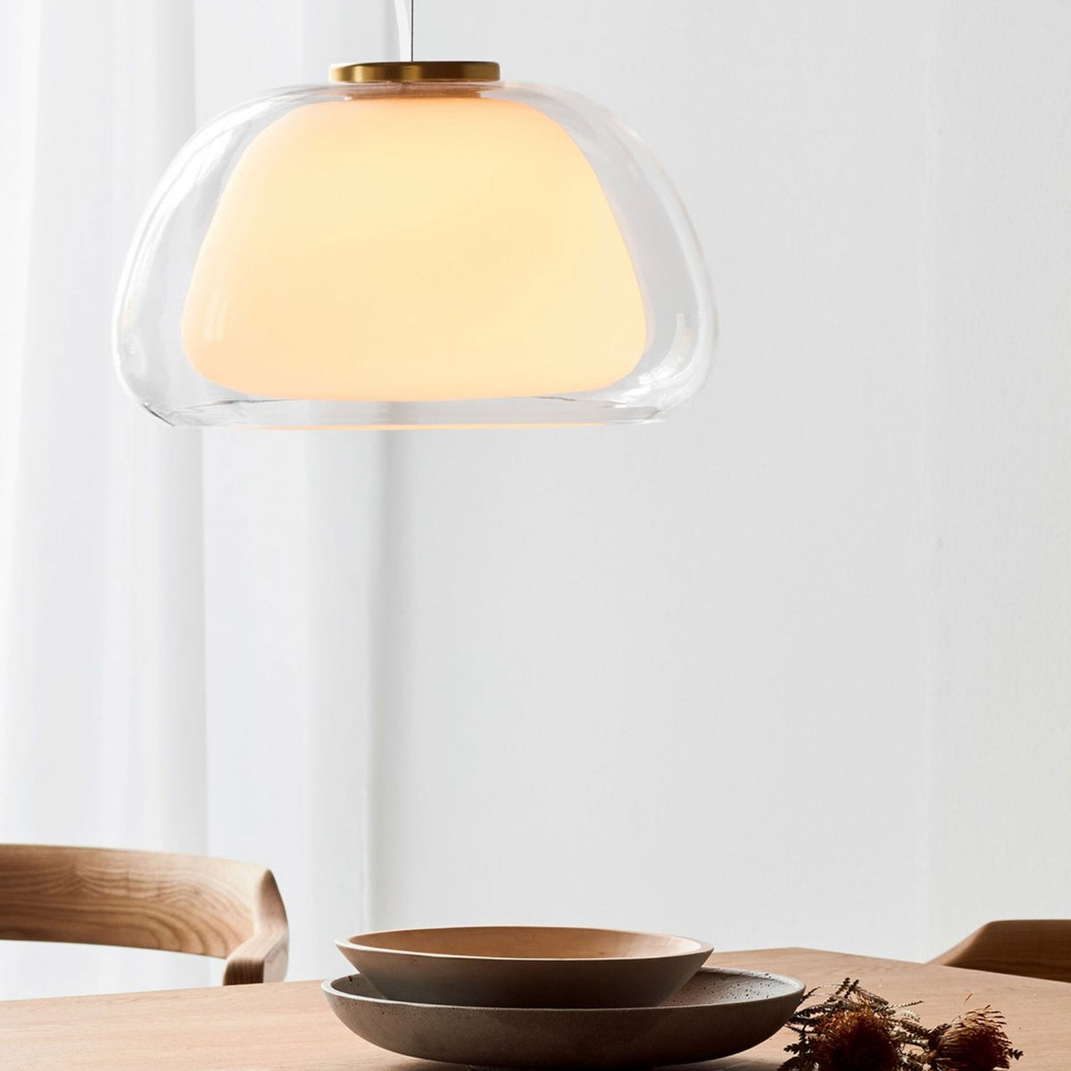 An illuminated pendant light hangs over a wooden table set with plates, in a bright room.
