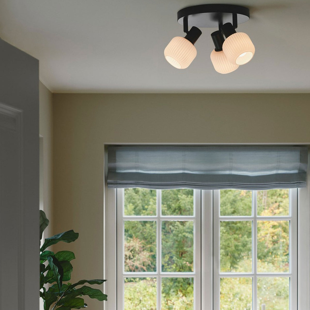 A black ceiling light with three adjustable white glass shades illuminates a bright room.