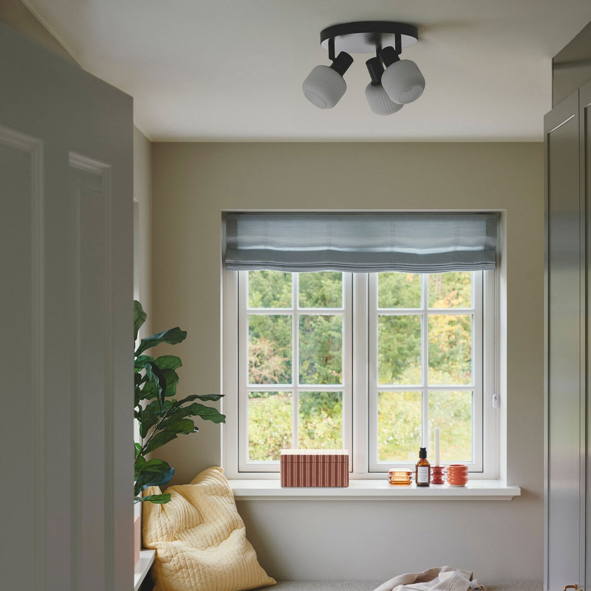 A black ceiling light with three white glass shades illuminating a windowed room.