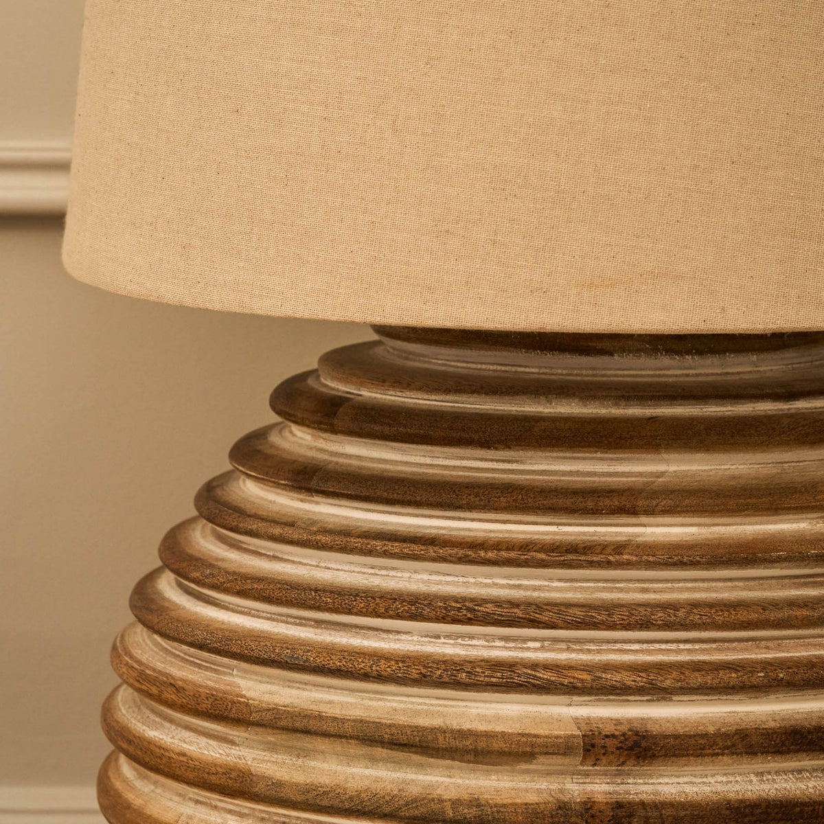 Close-up of a lamp with a beige fabric shade and a ribbed, light brown wooden base.