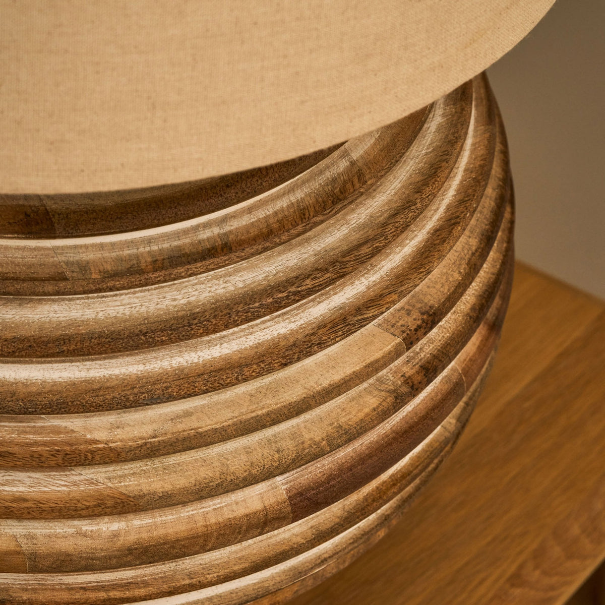 Close-up of a wooden lamp base with horizontal grooves and a light brown fabric shade.