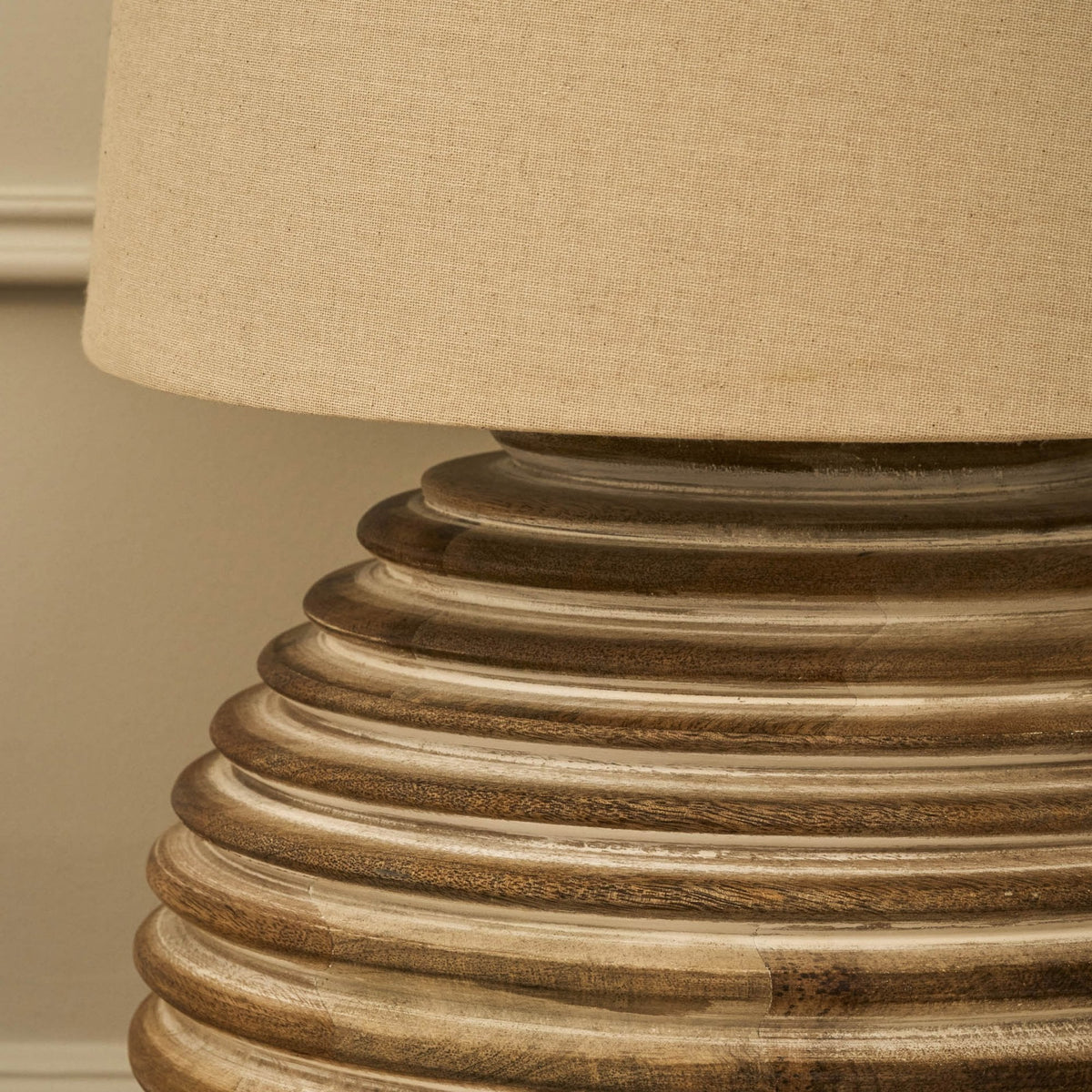 Close-up of a table lamp with a beige fabric shade and a ribbed, distressed wooden base.