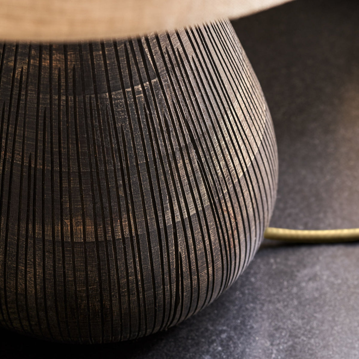 Close-up of a dark, textured lamp base with vertical grooves, on a dark surface.
