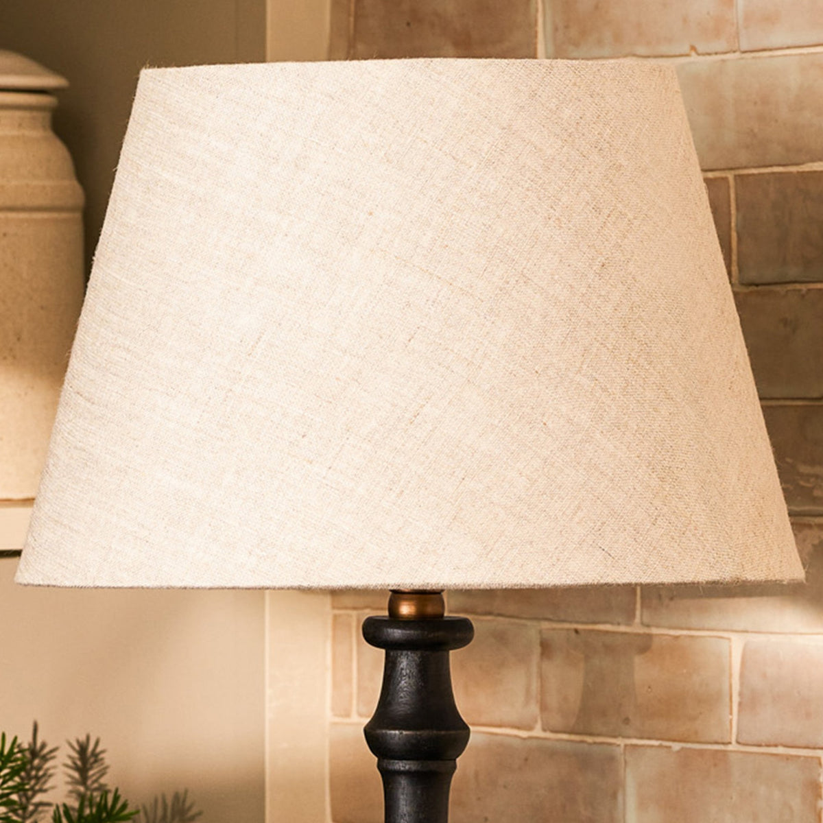 A close-up of a lamp with a light-colored fabric shade and a dark, carved base.