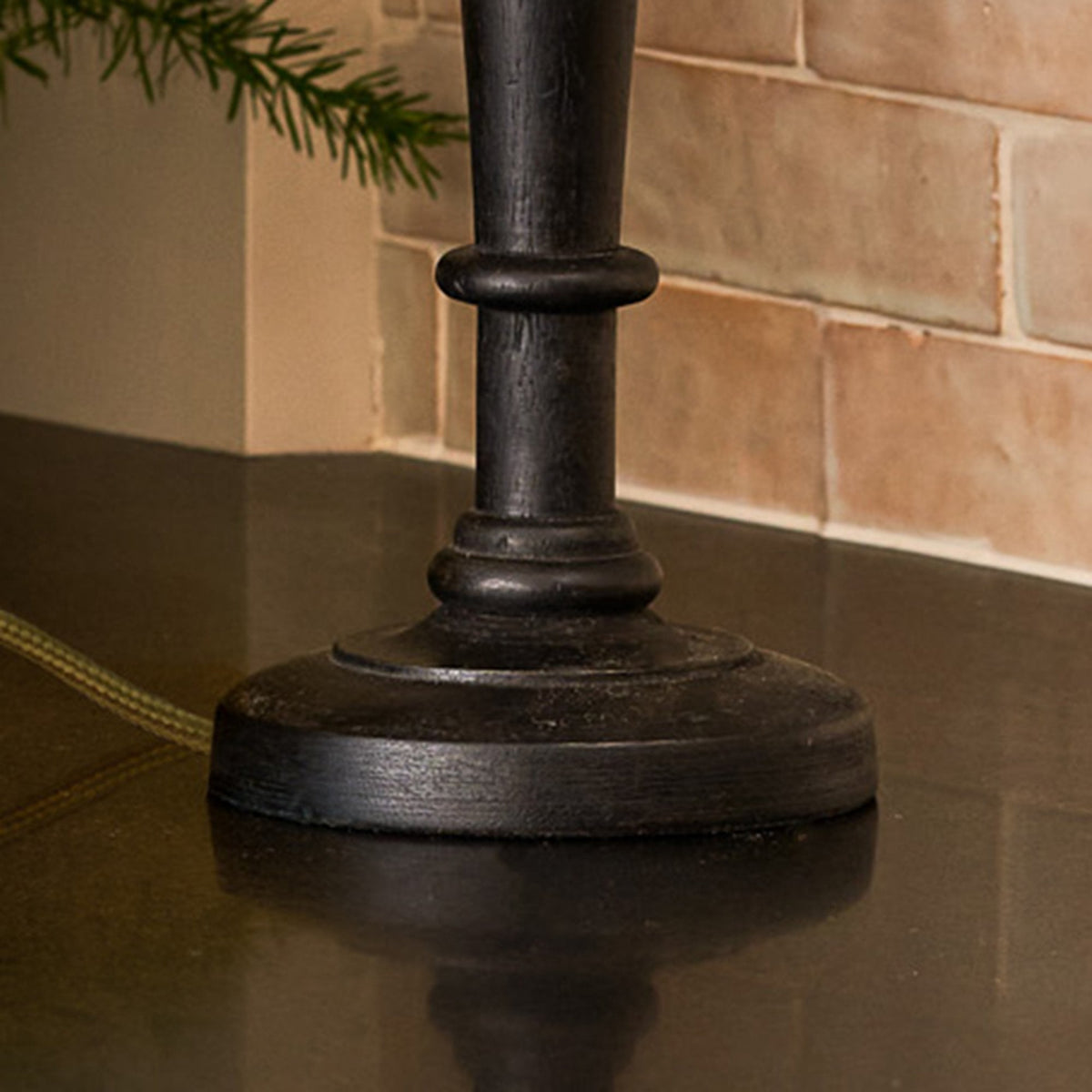 Close-up of a dark, distressed lamp base on a reflective surface, with a tiled wall in the background.