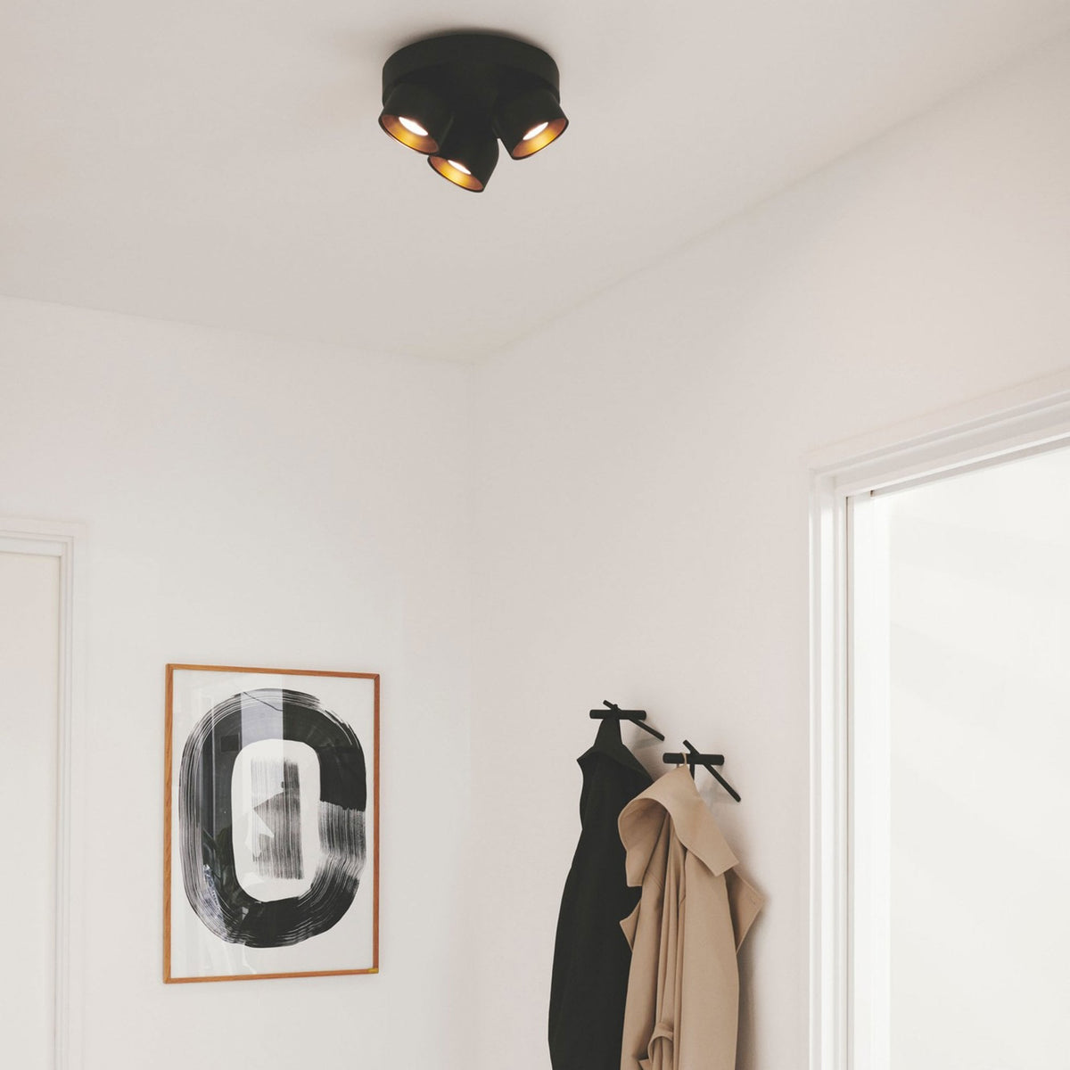 A black three-spot ceiling light illuminates a minimalist white hallway with a framed print.
