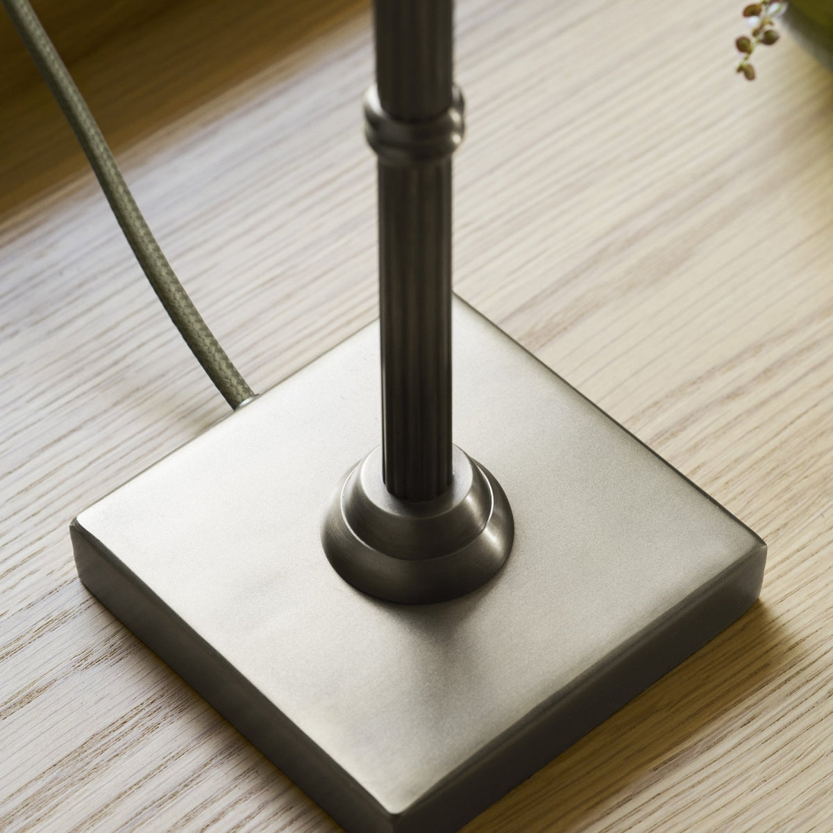 Close-up of a lamp base on a wooden surface. The base is square and made of brushed metal.