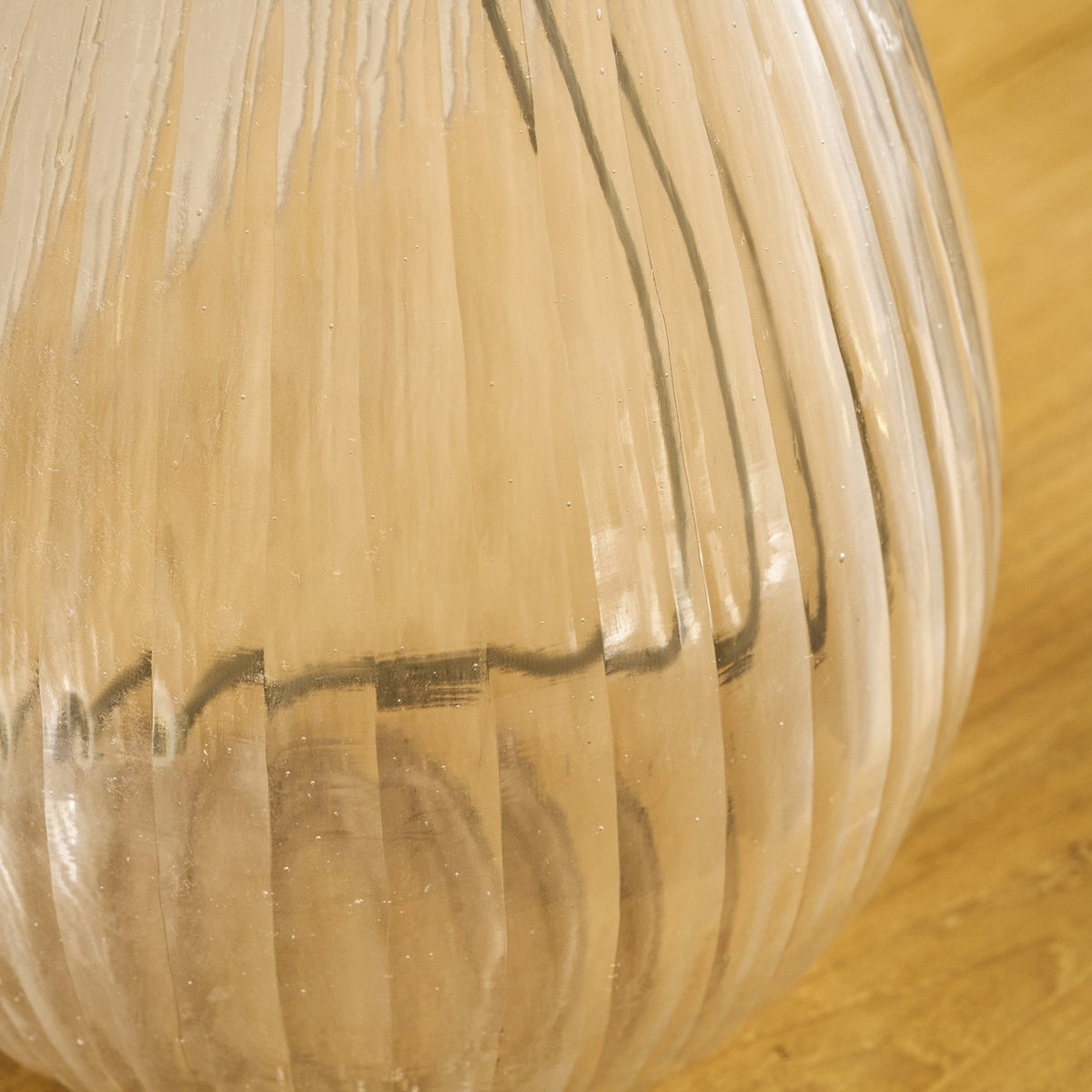 Close-up of a ribbed glass vase with a golden hue, showing vertical lines and subtle imperfections.