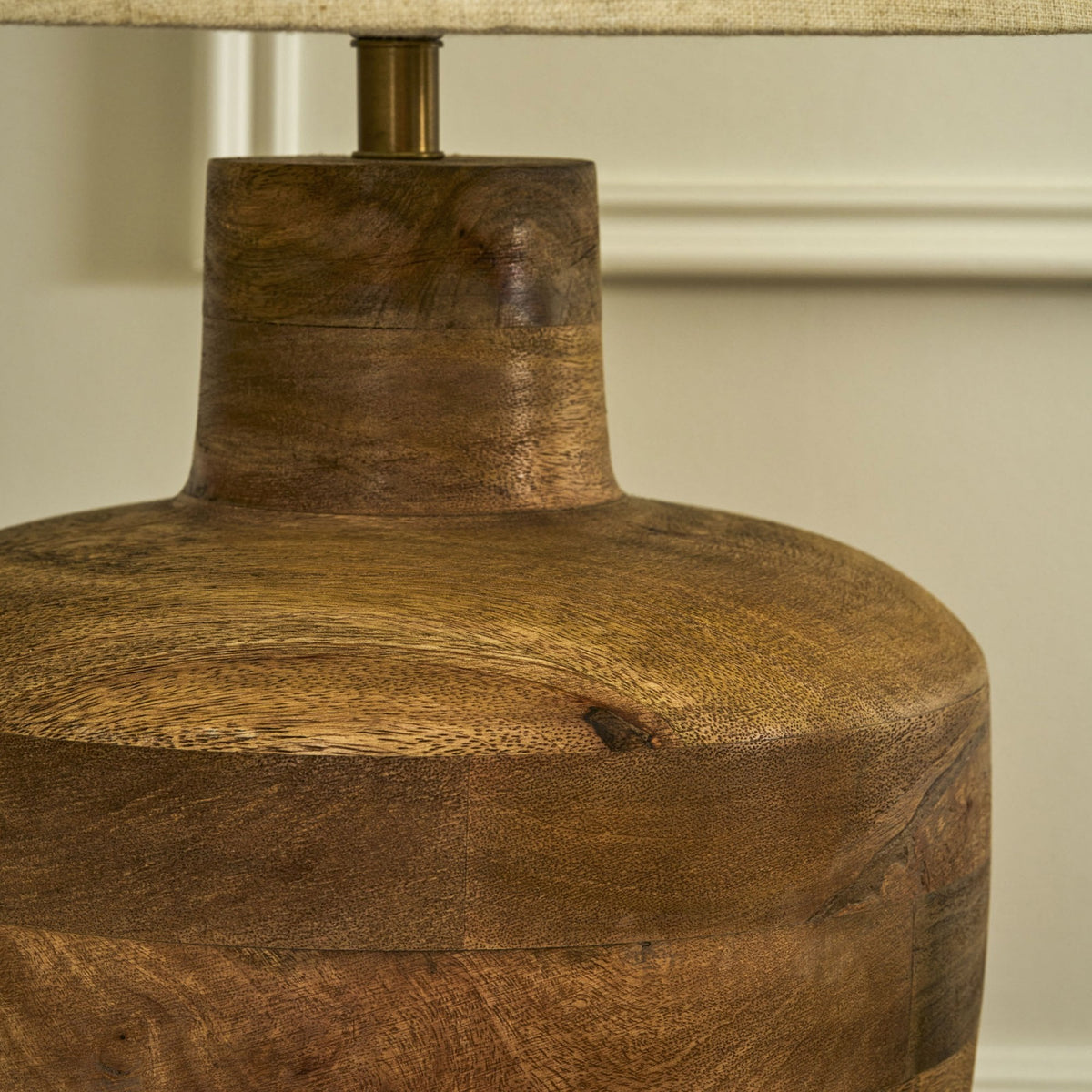 Close-up of a wooden lamp base with a textured fabric shade, showcasing natural wood grain and a brass stem.