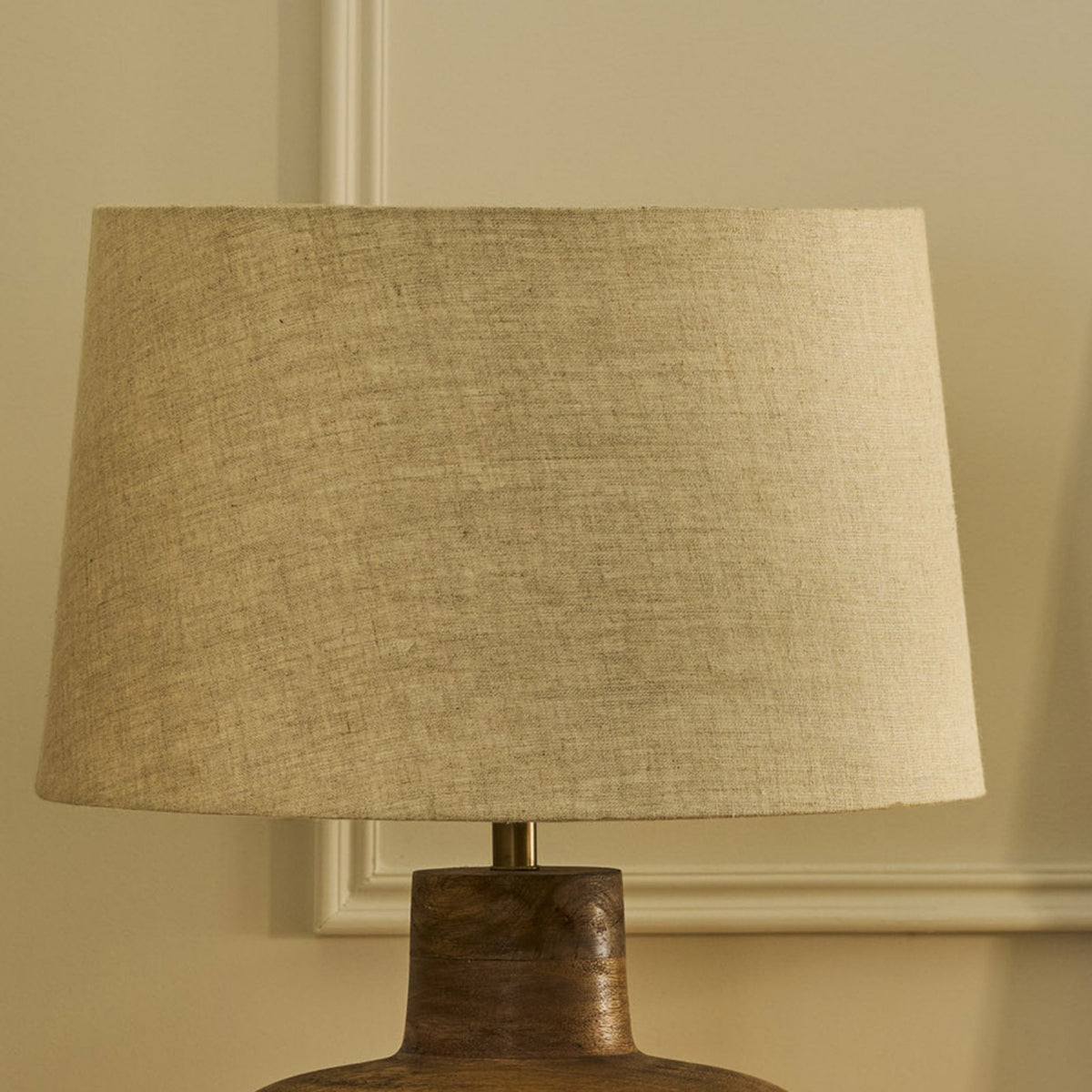 Close-up of a table lamp with a natural linen shade and a dark wooden base.