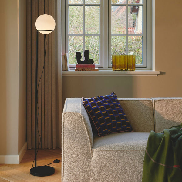 A black floor lamp with a white spherical shade illuminating a living room corner.