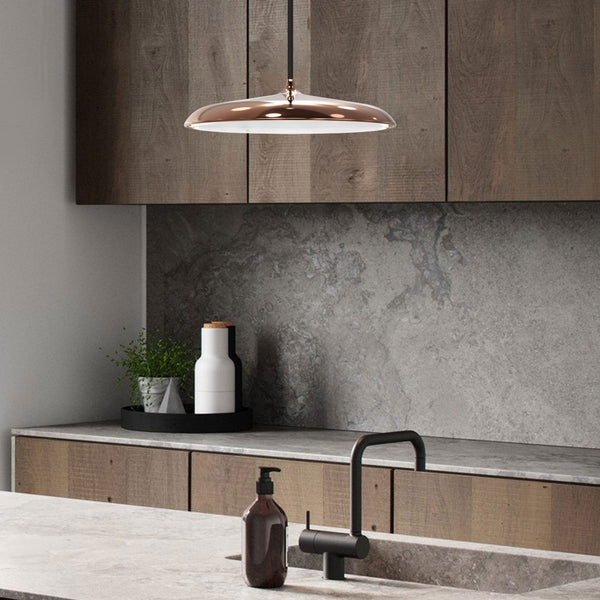 Copper finish pendant light in a modern kitchen with wooden cabinets and stone countertops.