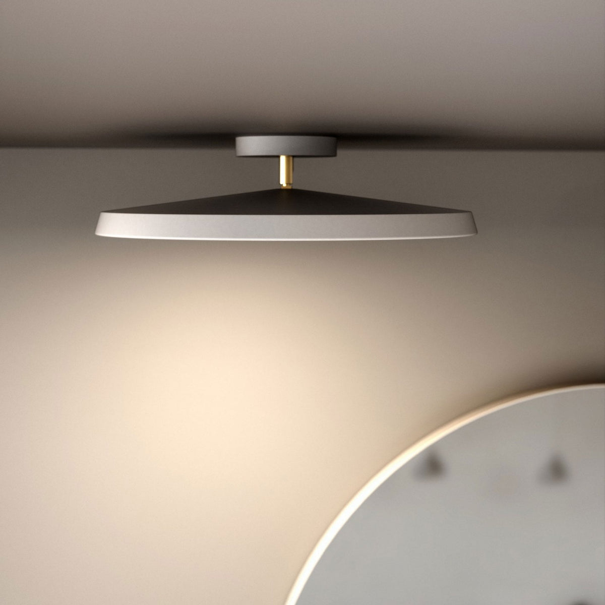 A black and white ceiling light with a gold stem, illuminating a wall and a mirror