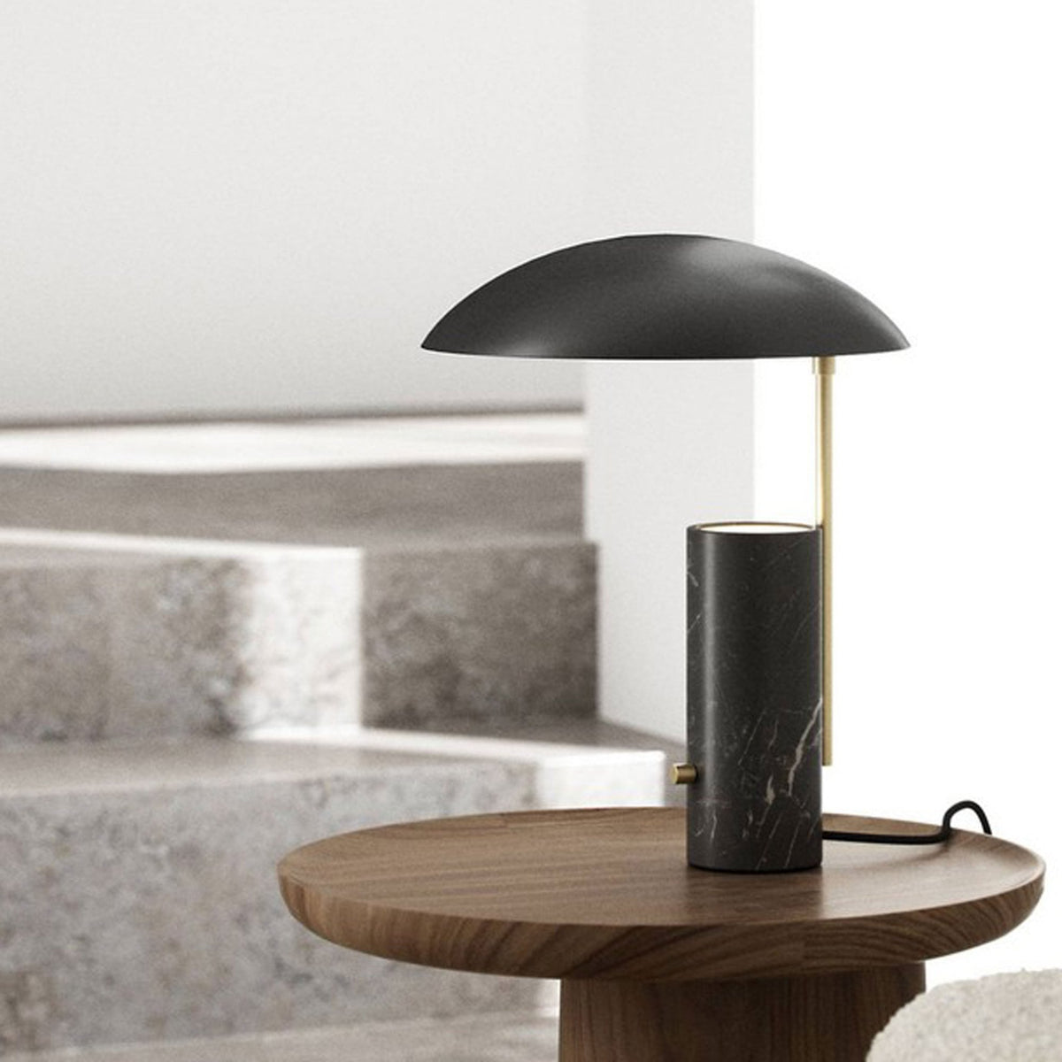 Table lamp on a wooden side table next to a sofa, with concrete stairs in the background.