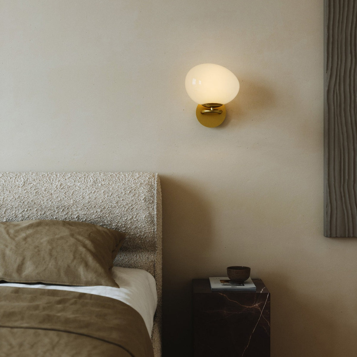 A white orb wall light with a brass base illuminates a bedroom setting.