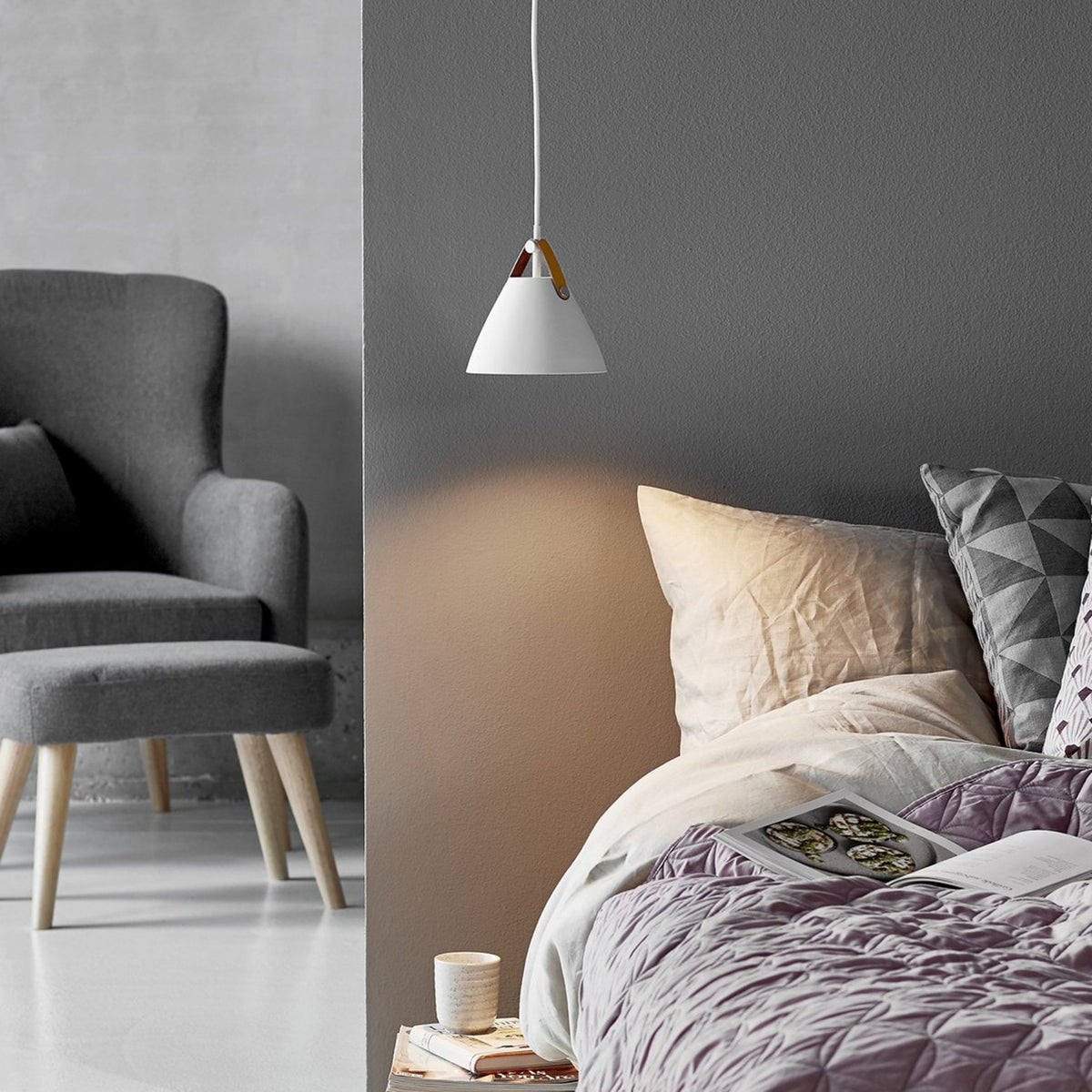 A white pendant light with a tan leather strap hangs above a bed.