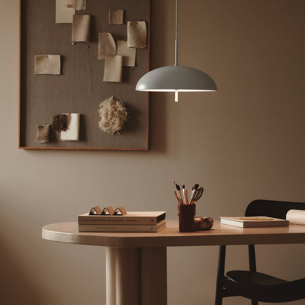 A grey pendant light illuminating a light wooden table in a room with a brown wall.