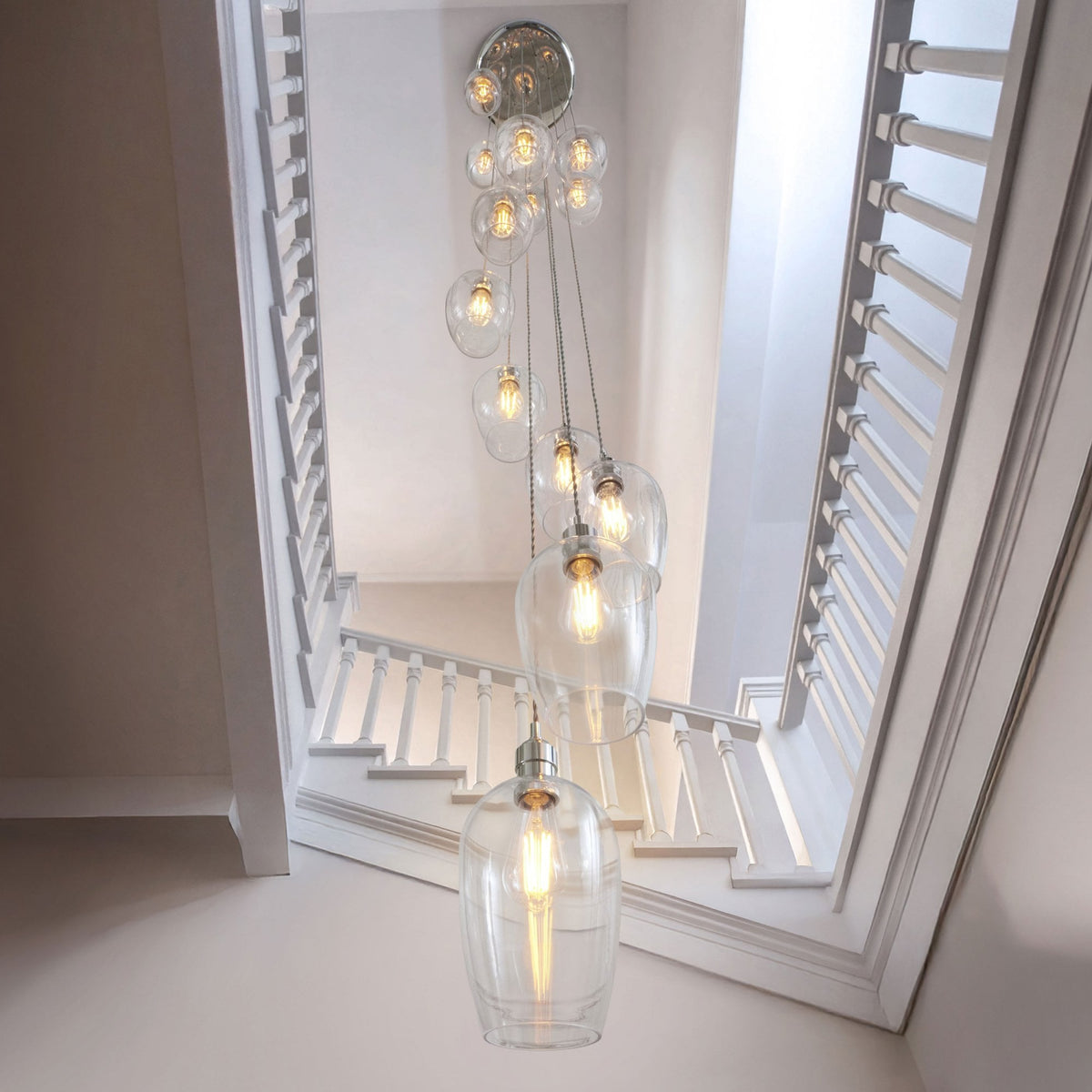Looking down into a stairwell at a multi-pendant light fixture with clear teardrop shades, creating a warm glow.