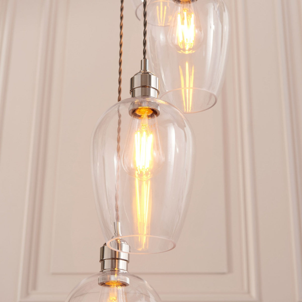 Detailed view of the clear teardrop-shaped light shades with internal filament bulbs, against a paneled wall.