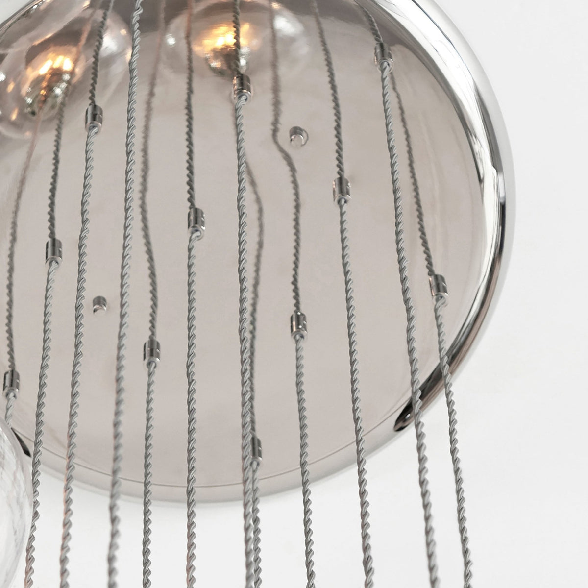 Close-up of the polished chrome ceiling plate of the multi-pendant light, with various hanging wires.