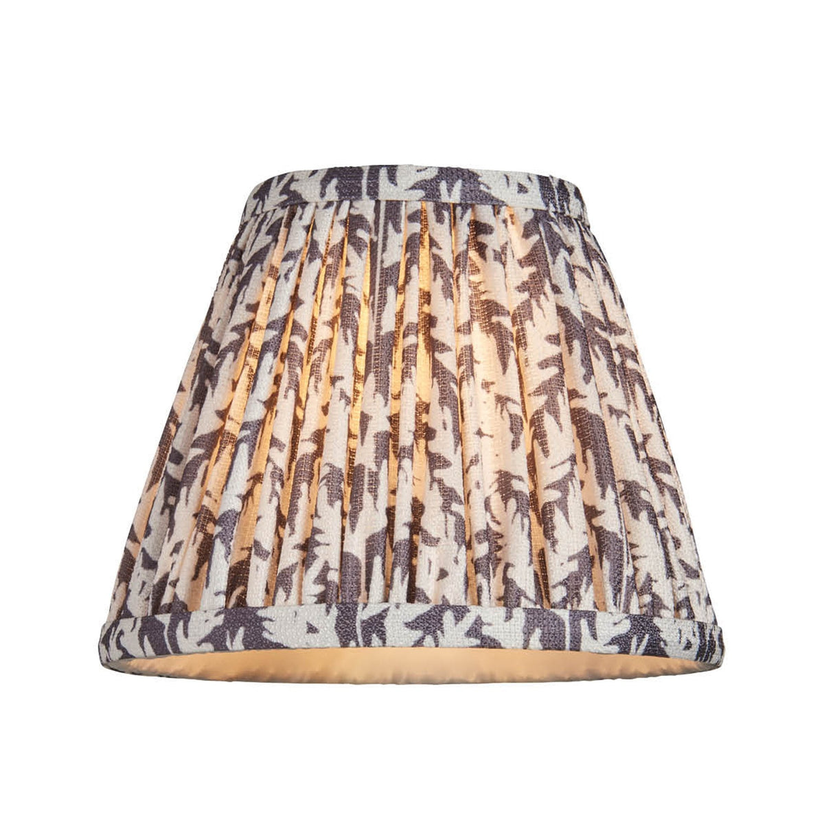 A pleated lampshade with a light background and dark leaf-like patterns, illuminated from within.