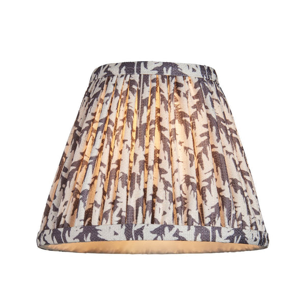 A pleated lampshade with a light background and dark leaf-like patterns, illuminated from within.