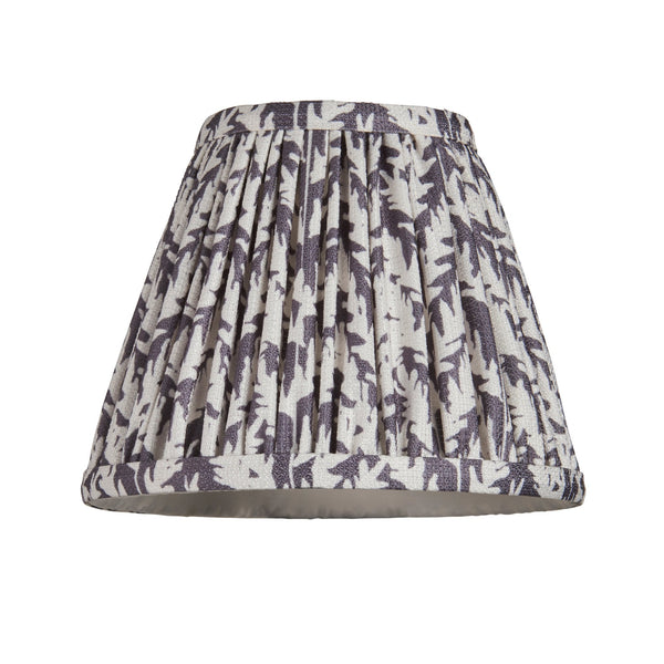A pleated lampshade with a light background and dark leaf-like patterns, unlit.