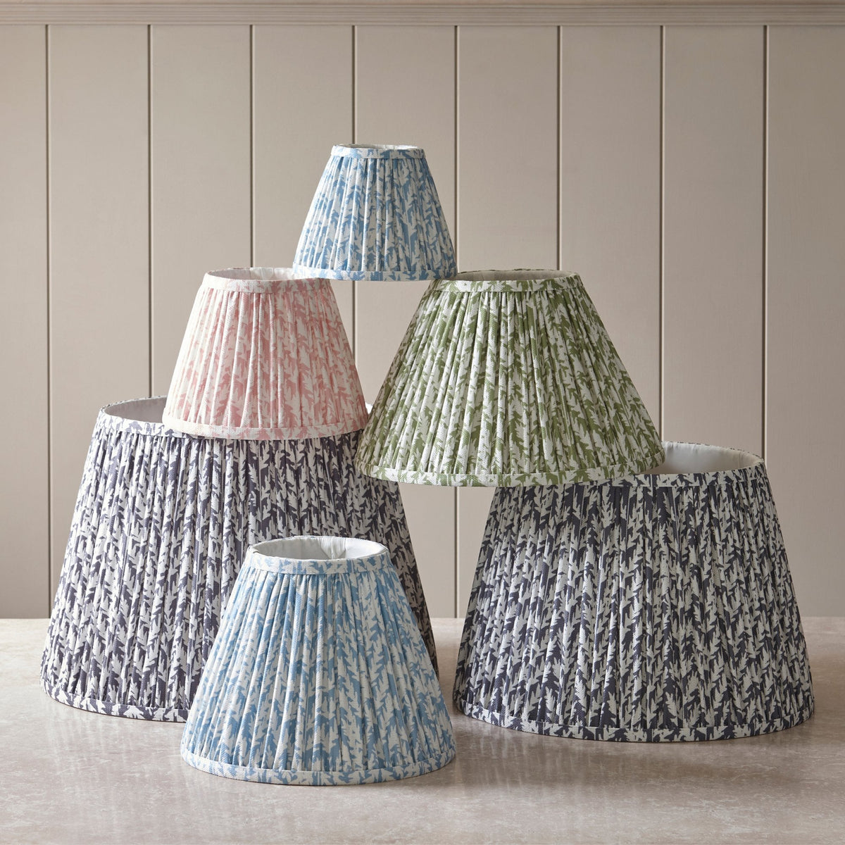A collection of pleated lampshades in various colors and sizes, stacked artfully.