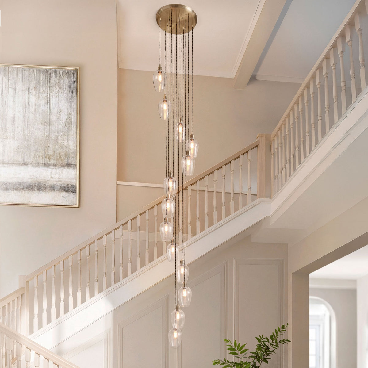 A long, spiral chandelier with multiple glass pendants hangs in a foyer next to a staircase.