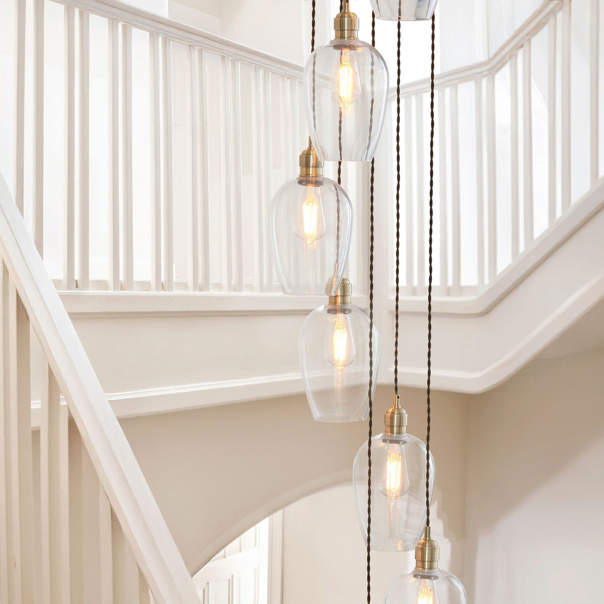 Five glass pendant lights of a spiral chandelier hang next to a white wooden staircase.