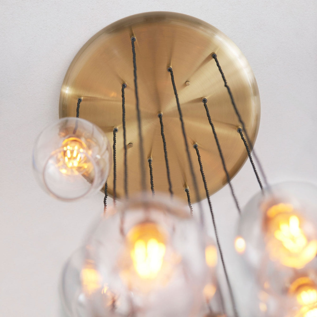The brass ceiling plate of a spiral chandelier with multiple dangling light cords and glass pendants.