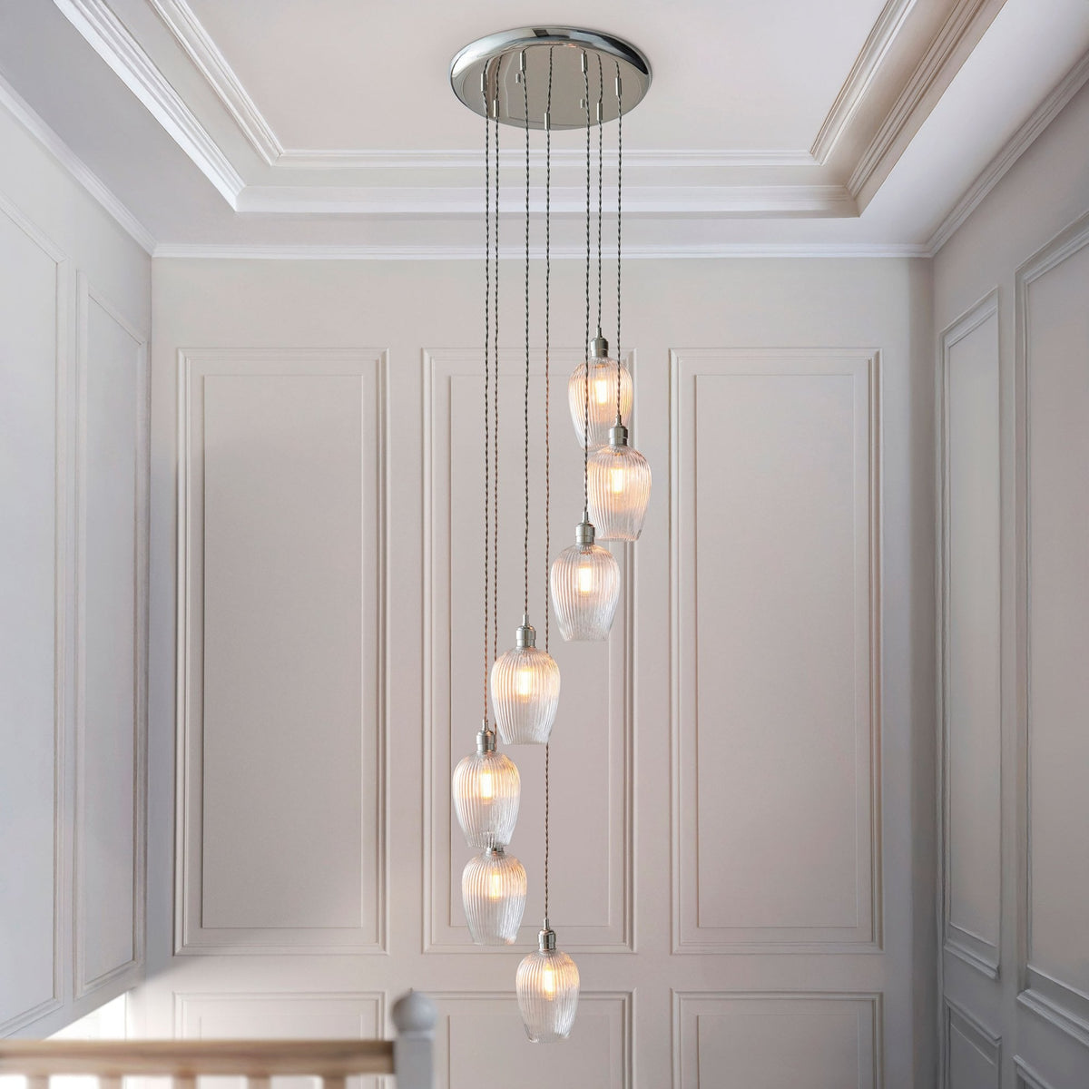 A contemporary multi-light pendant hangs in a hallway, illuminating the space with soft, ambient light.