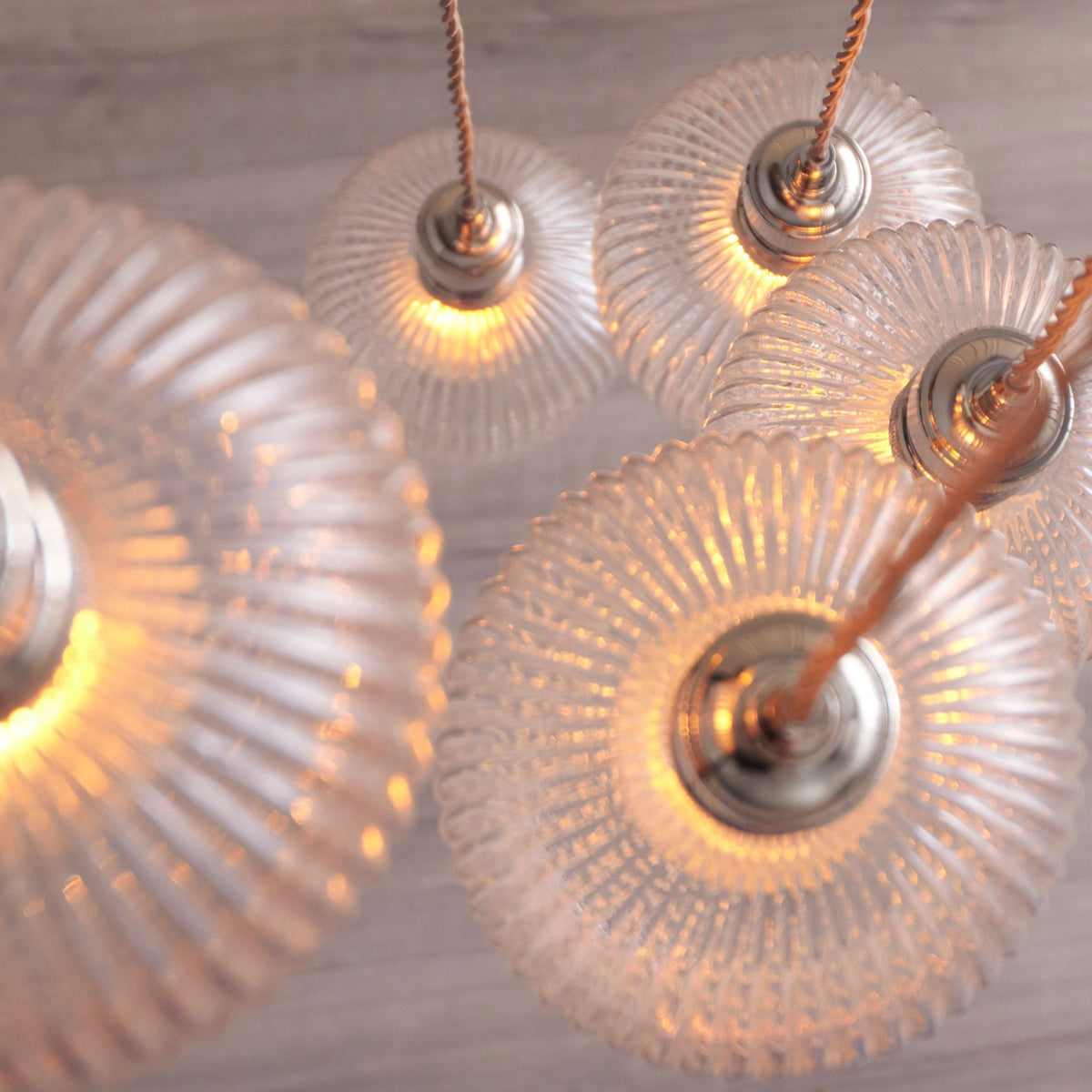 Close-up top view of clear ribbed glass shades from a multi-light pendant, showcasing intricate details and warm illumination.