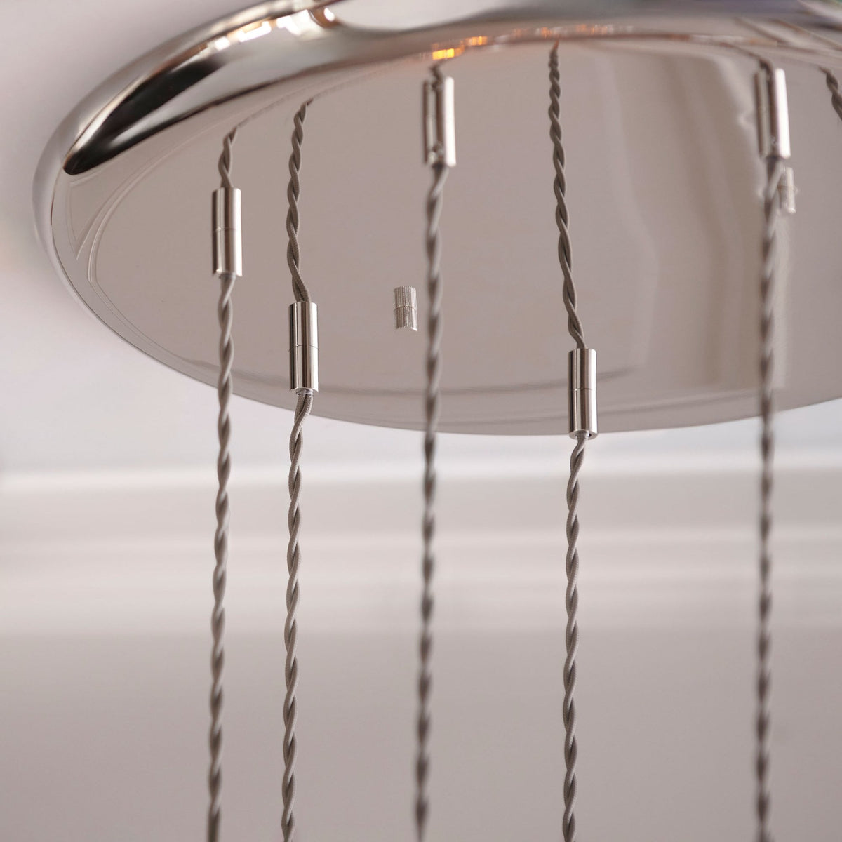 A close-up of the polished chrome ceiling plate of a multi-light pendant, featuring neatly arranged suspension cables.