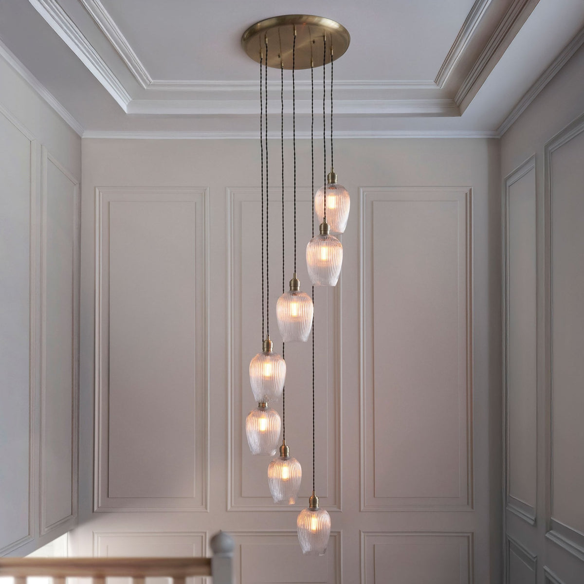 A multi-pendant cluster light with seven glass shades, hanging at varying lengths above a staircase.
