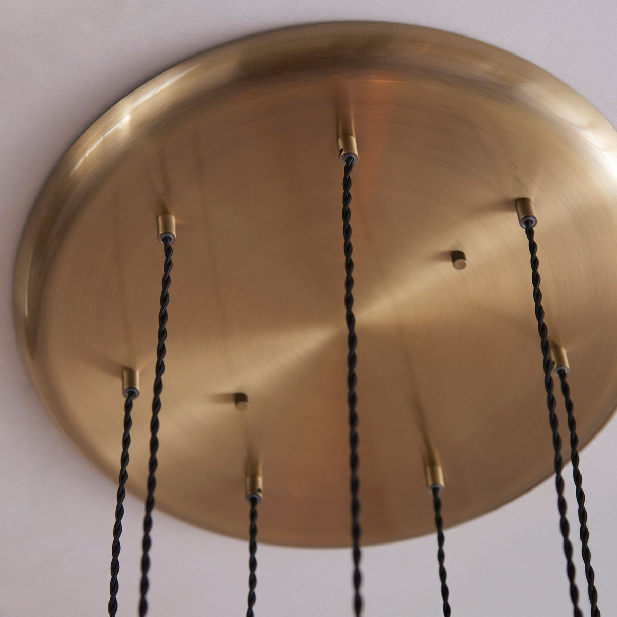 A close-up of the brass ceiling plate from which the seven pendant lights suspend, featuring multiple cords.