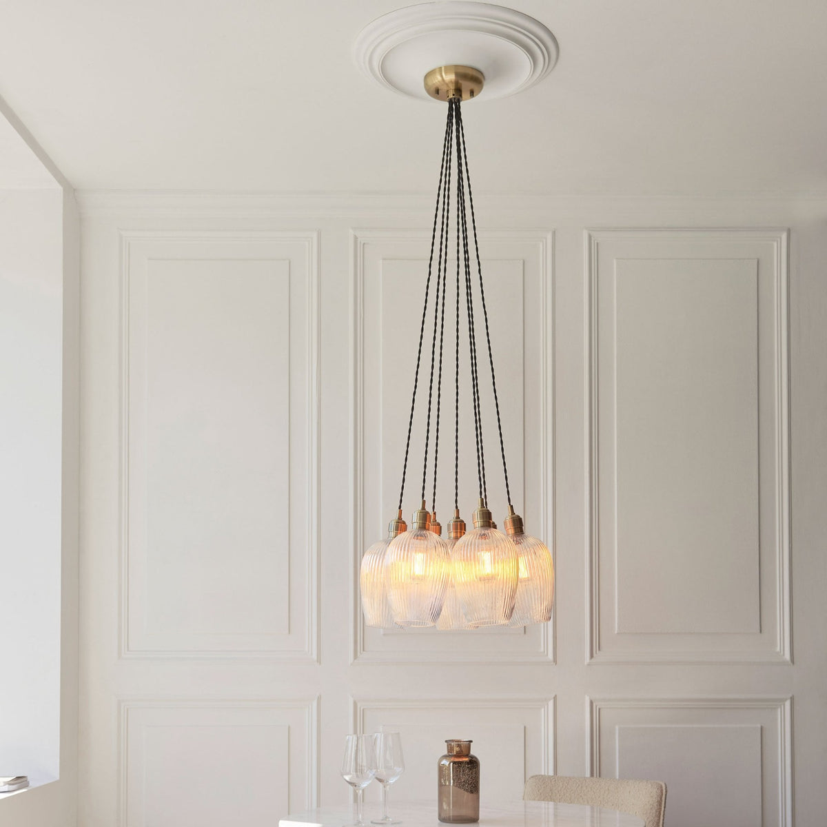 A full view of the Volia Glass Chandelier, featuring five ribbed glass shades, against a white paneled wall and ceiling.