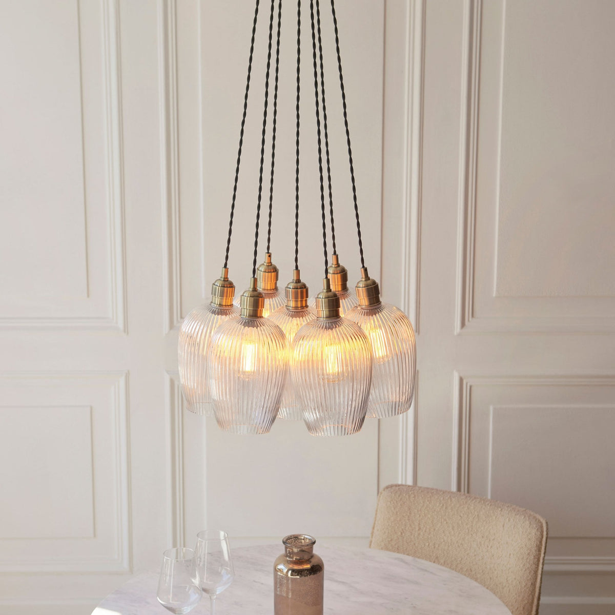 A full view of the Volia Glass Chandelier, featuring five ribbed glass shades, with a subtle glow, above a white table.