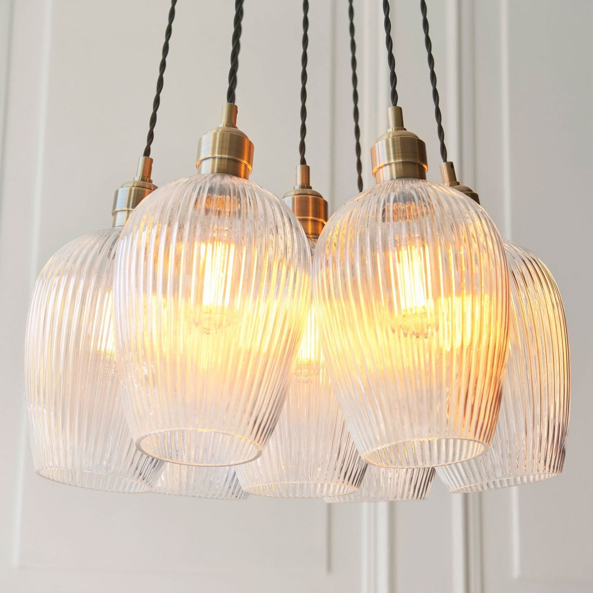 A close-up view of the Volia Glass Chandelier, highlighting the five ribbed glass shades with visible glowing bulbs.