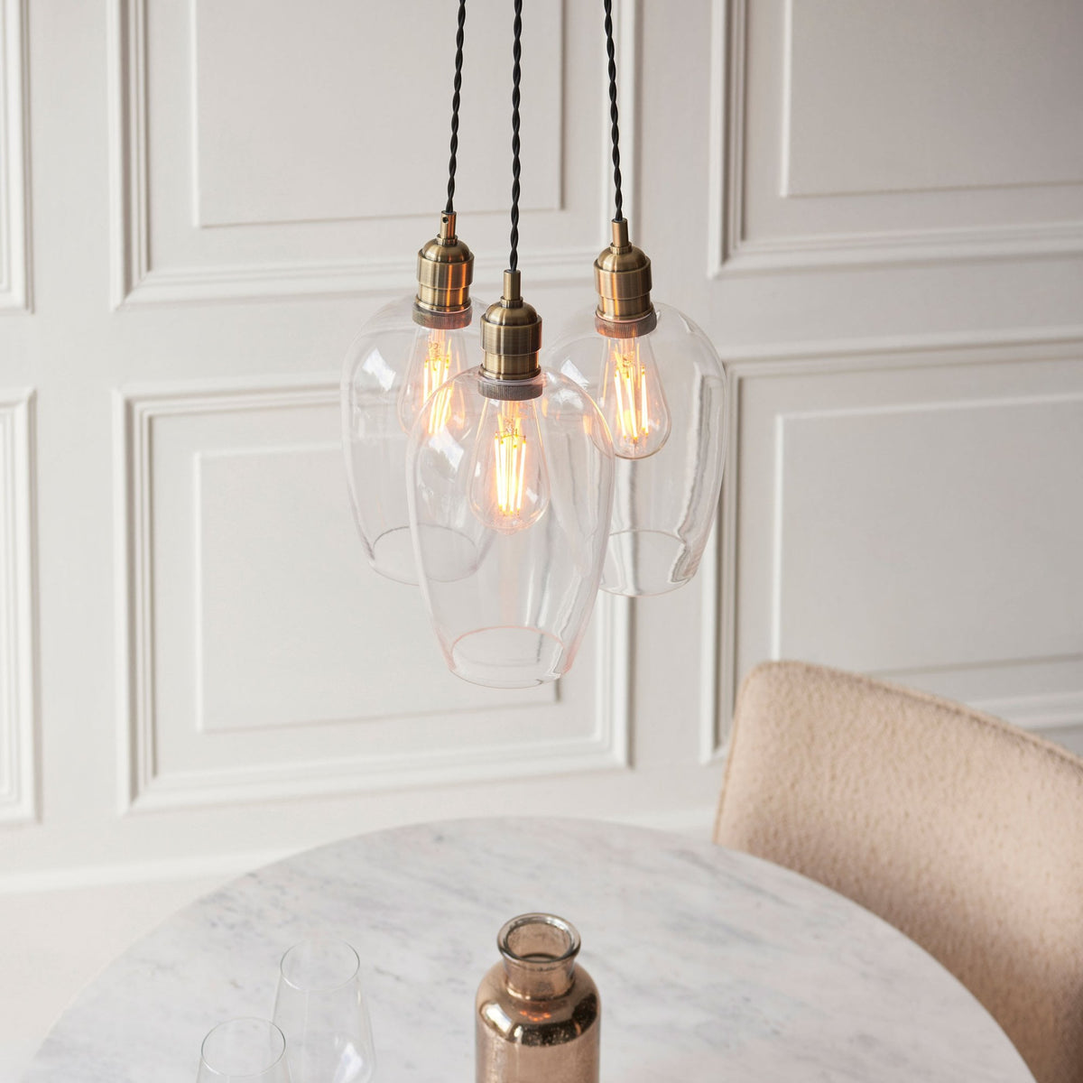 Close-up of three clear glass pendant lights with brass fittings hanging above a white marble table.