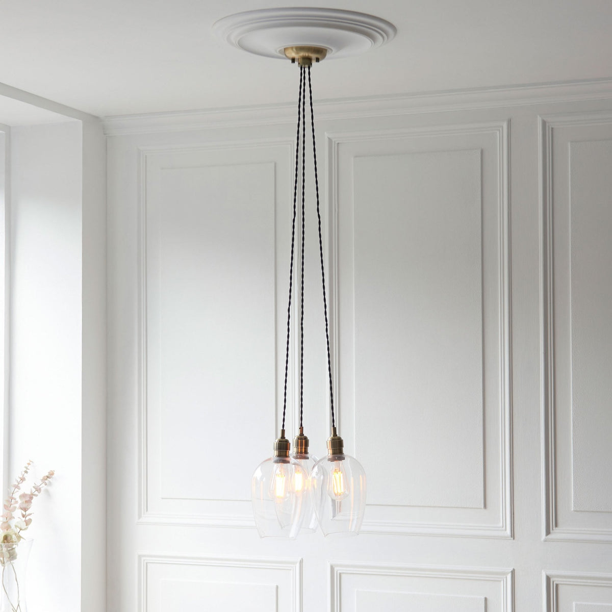 Three clear glass pendant lights with brass fittings hang from a white ceiling medallion in a modern room.