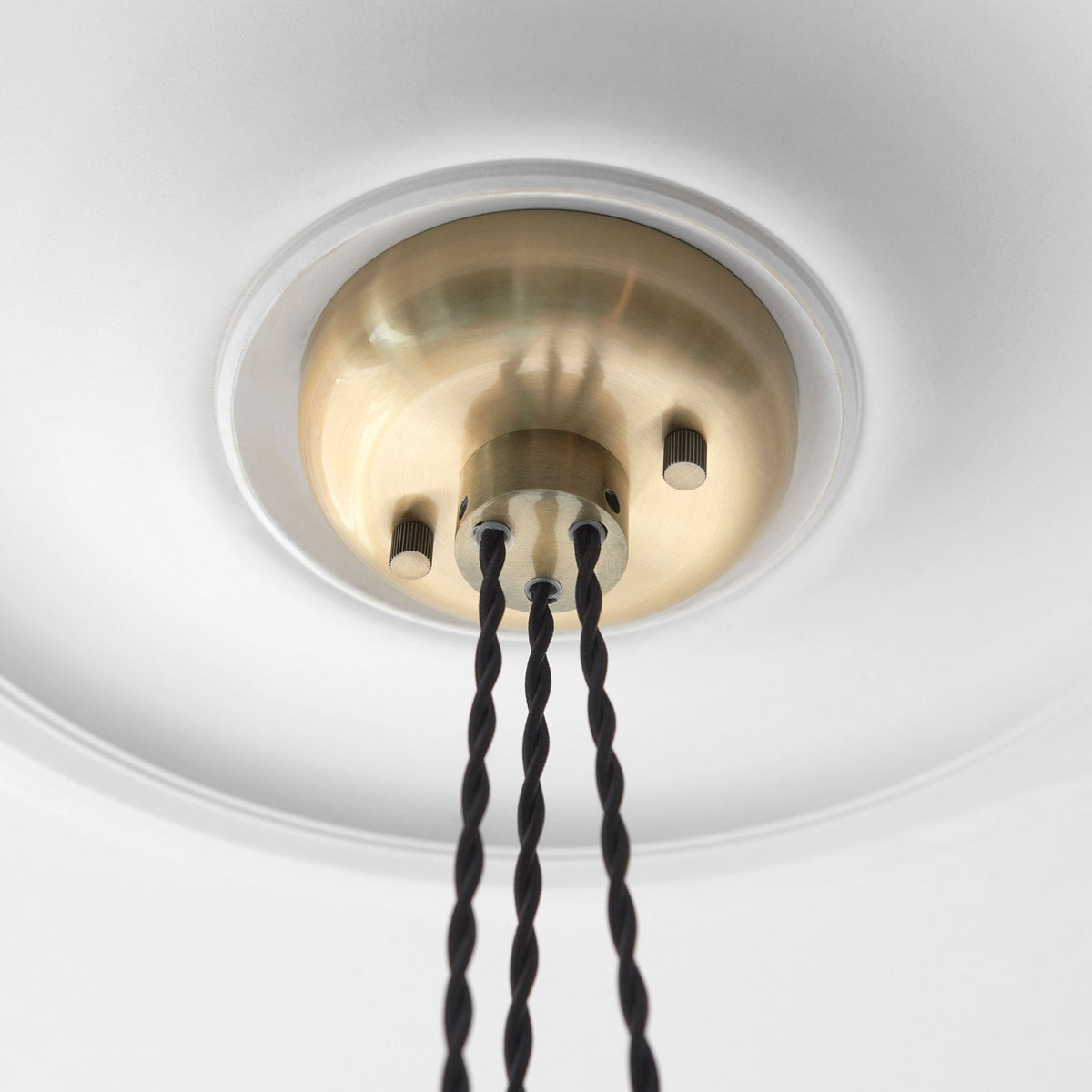 Close-up of the brass ceiling plate and three braided cords of the pendant lights.