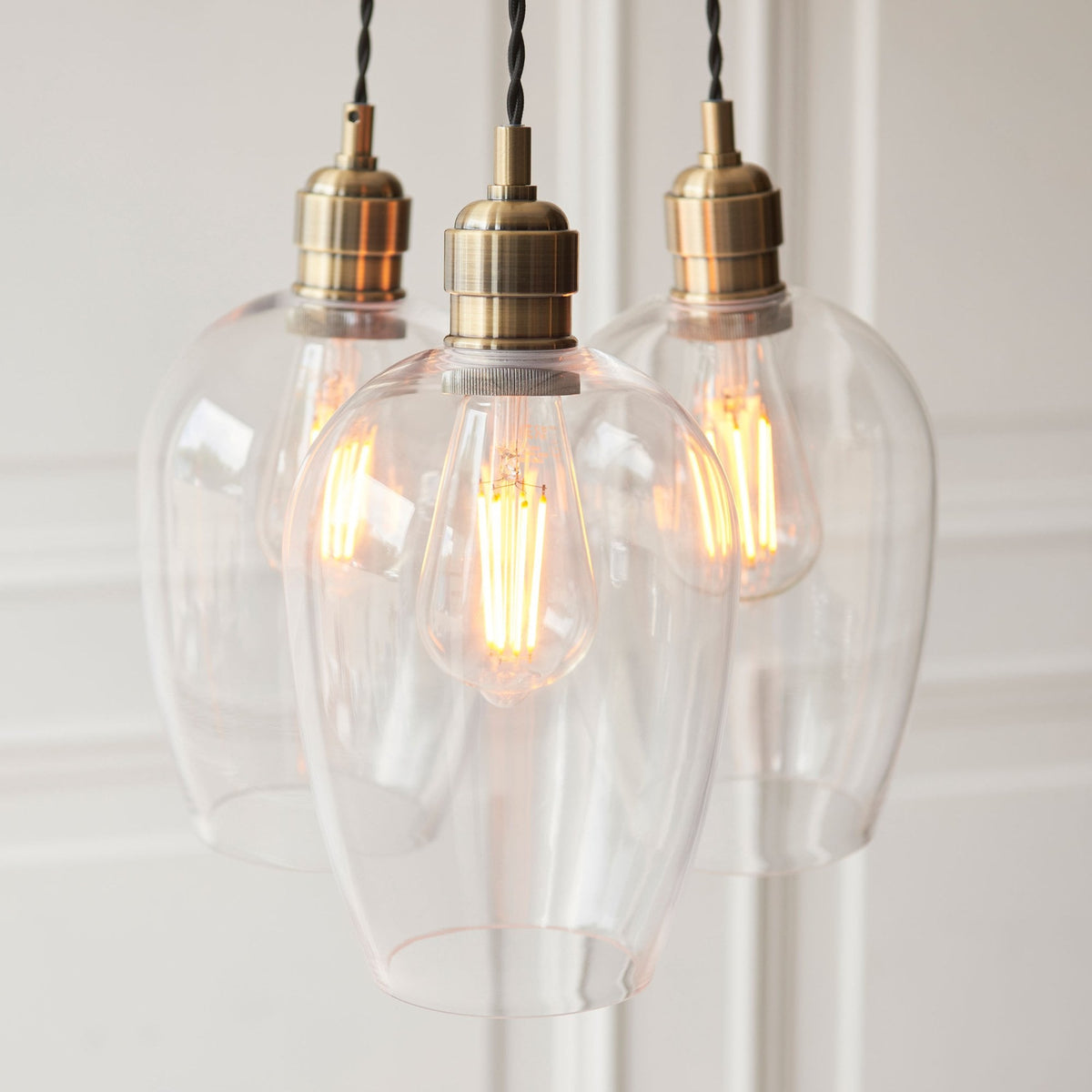 Detailed view of the three clear glass shades and brass bulb holders, showing the exposed filaments.