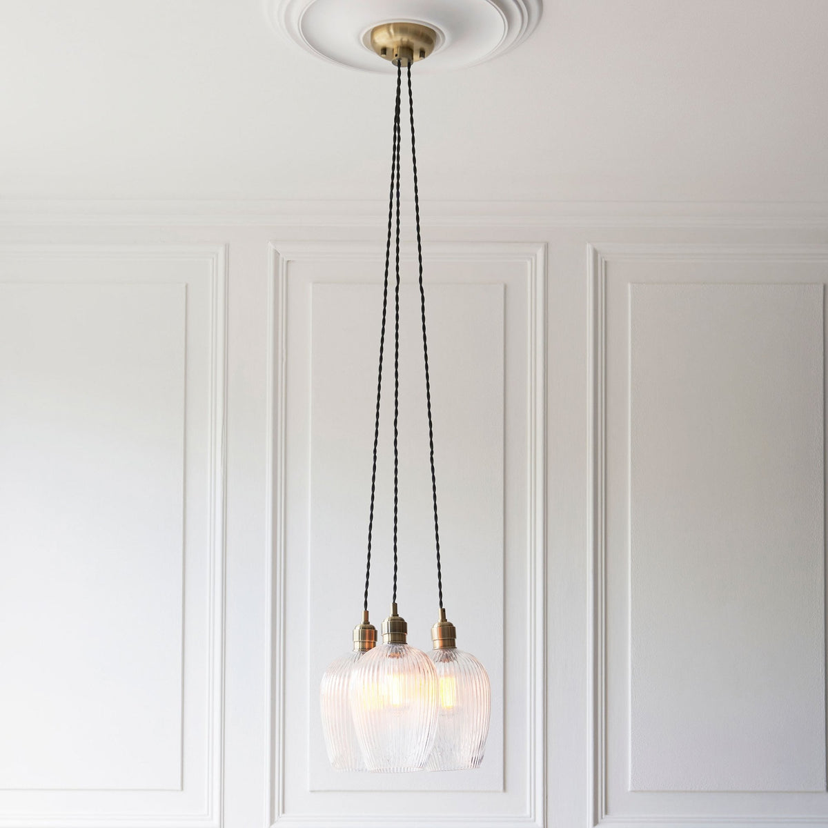 A cluster of three ribbed glass pendant lights with brass ceiling rose against a white ceiling.
