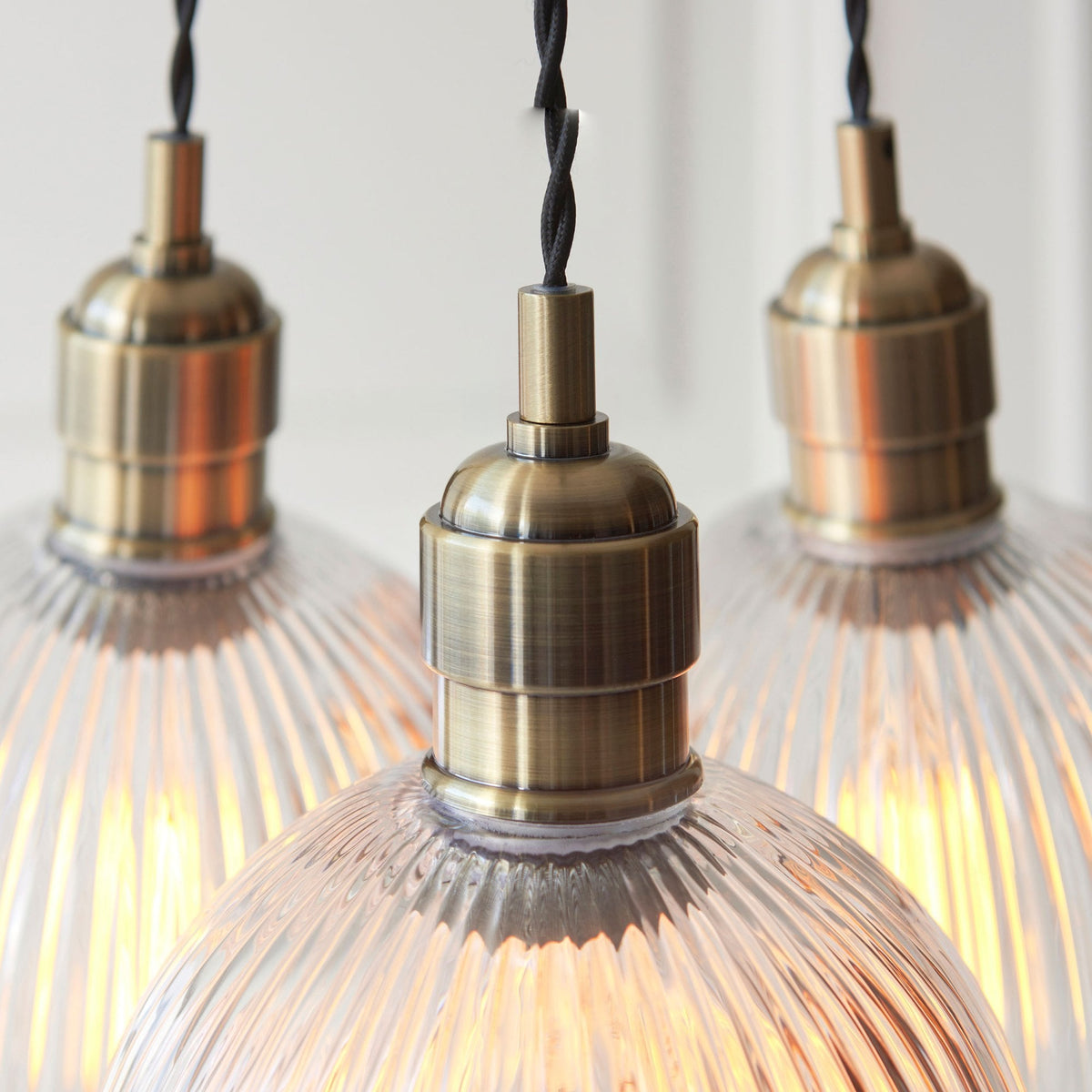 Close-up of three ribbed glass pendant shades with glowing bulbs and brass top fittings.