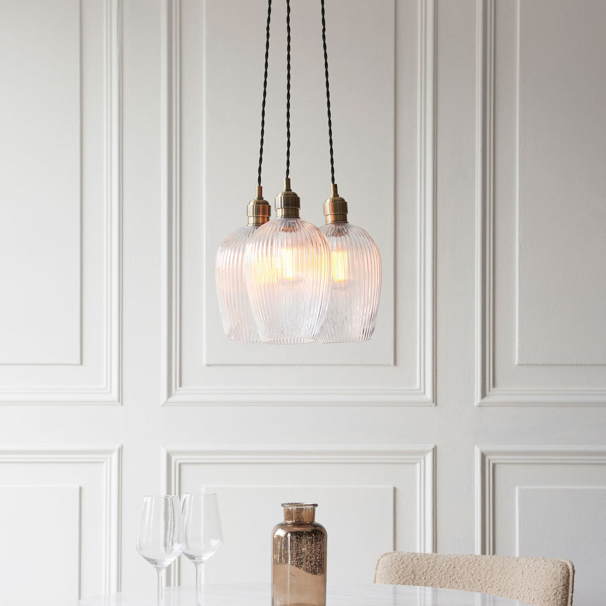 Three ribbed glass pendant lights illuminate a dining area with a marble table and a decorative vase.