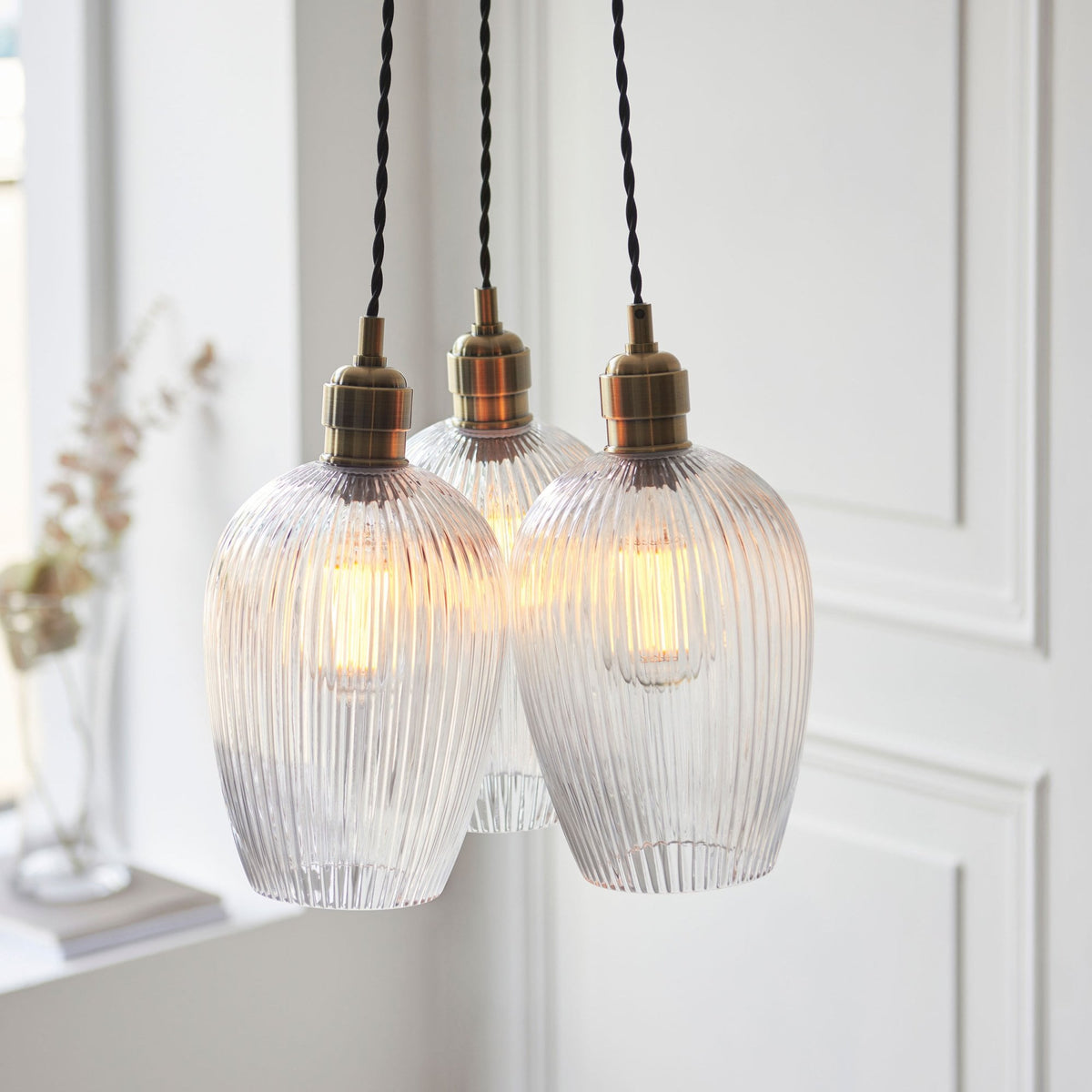 Three ribbed glass pendant lights with brass details hang illuminated in a home setting.